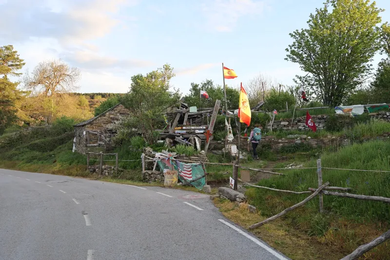 Stone building with flags, a person walking nearby, surrounded by greenery and a winding road.