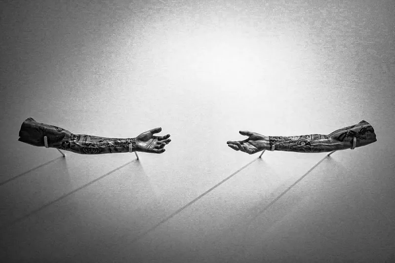 Two outstretched tattooed arms, positioned parallel on a plain surface with shadows extending behind them.