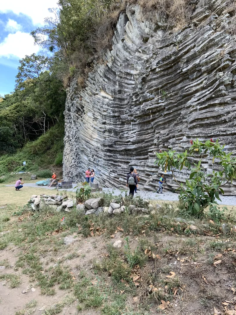 A layered rock formation with people exploring the area and greenery in the foreground.