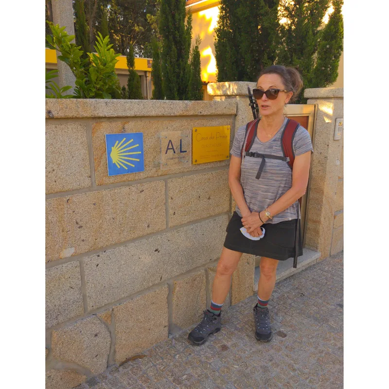 A woman in a striped shirt and backpack stands by a stone wall displaying signs for "Casa do Provi" and "AL.