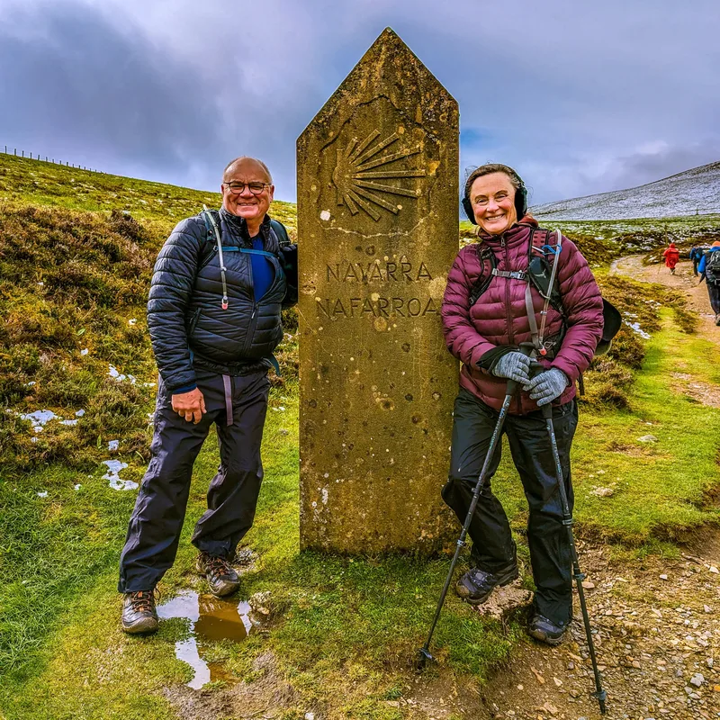 Two people stand smiling beside a stone marker inscribed with "NAVARRA NAFARROA" on a grassy trail.