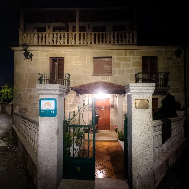 A stone house at night with a lit entrance, green gate, and balconies above.