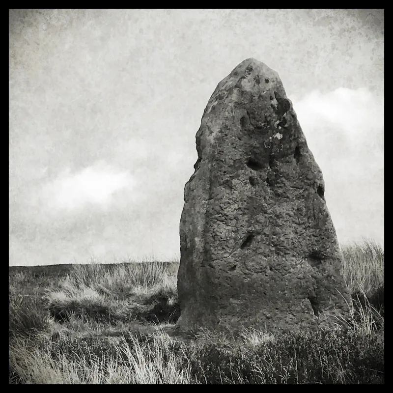 A large, upright stone monolith stands in a grassy field under a cloudy sky.