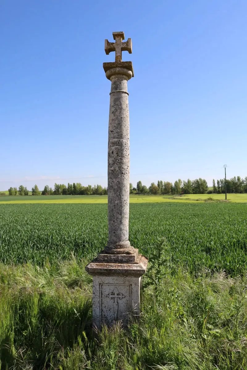 A tall stone pillar with a cross on top, surrounded by green fields under a clear blue sky.