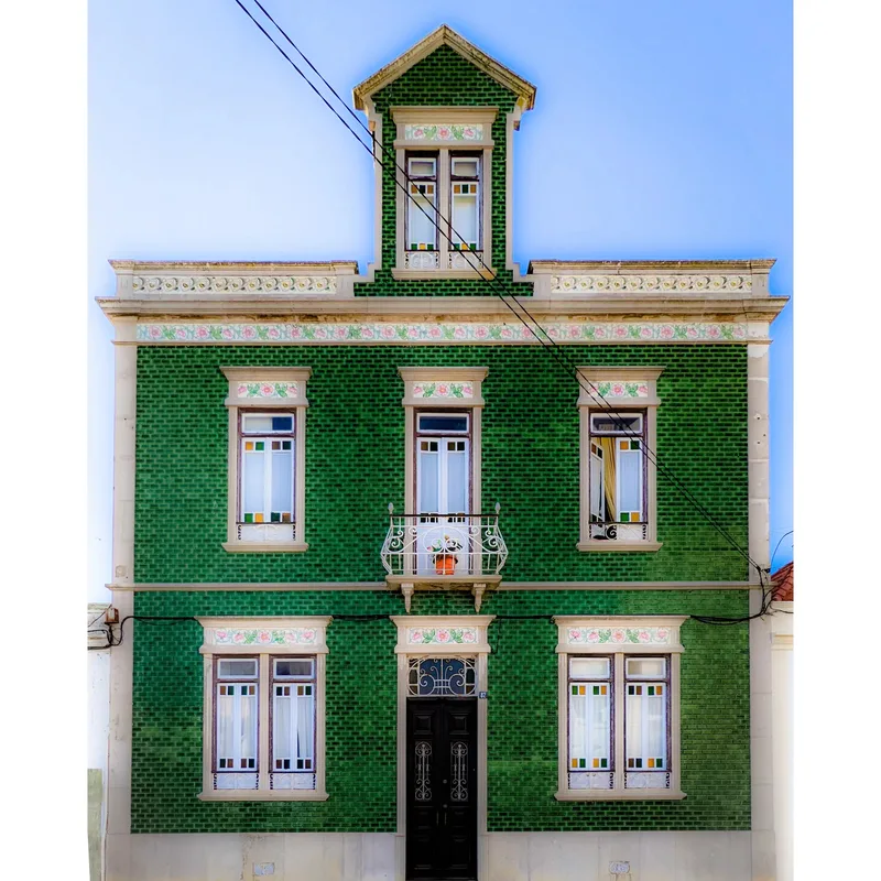 Green and white decorative building with a balcony, multiple windows, and a black door, set against a clear blue sky.