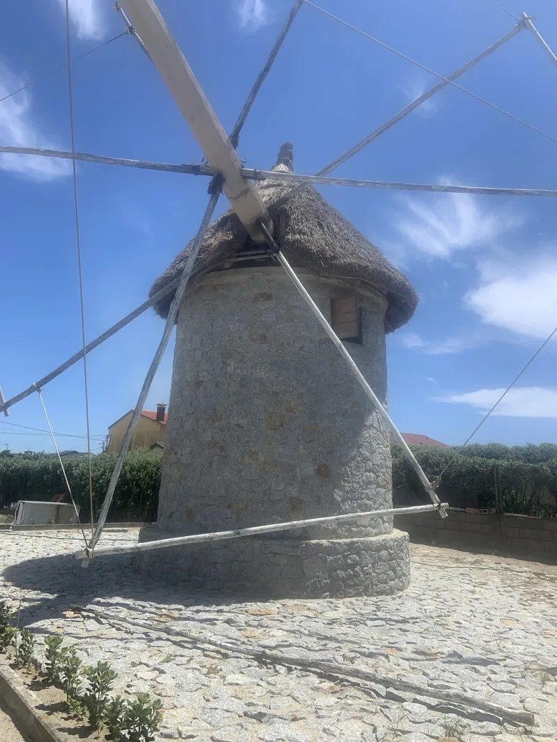 A stone windmill with a thatched roof, surrounded by a cobblestone ground and blue sky.