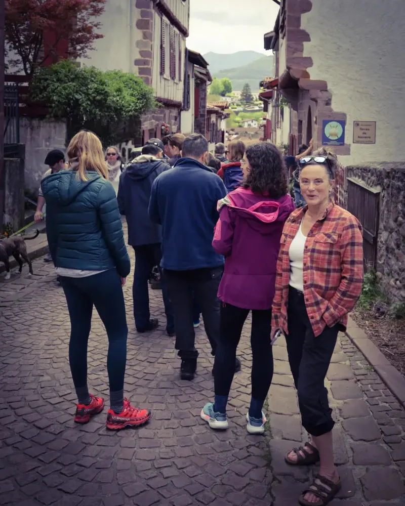 A narrow cobblestone street with a group of people walking, and two women facing the camera, one in a plaid shirt.